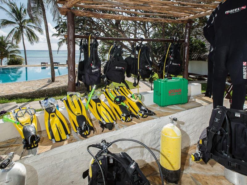 Duikuitrusting met vinnen en wetsuits bij een zwembad en palmbomen.