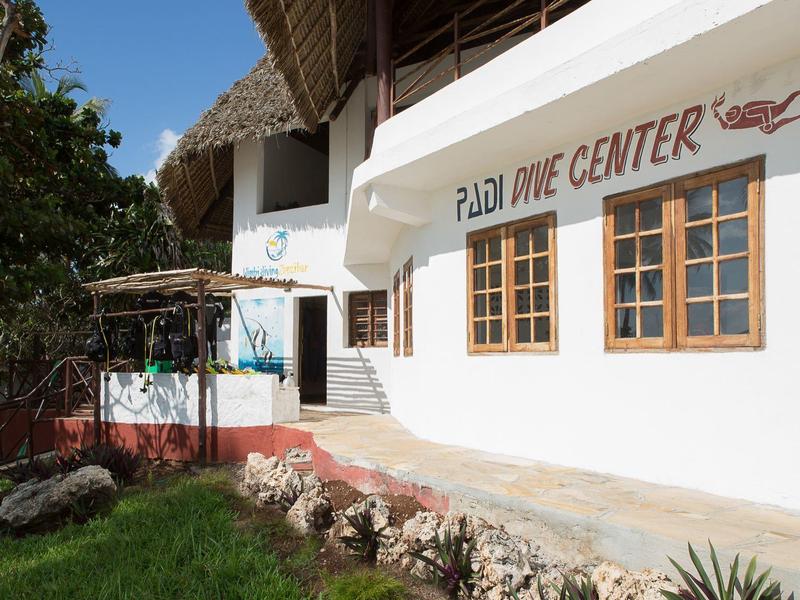 Wit duikcentrum met houten ramen en rieten dak in een tropische omgeving.
