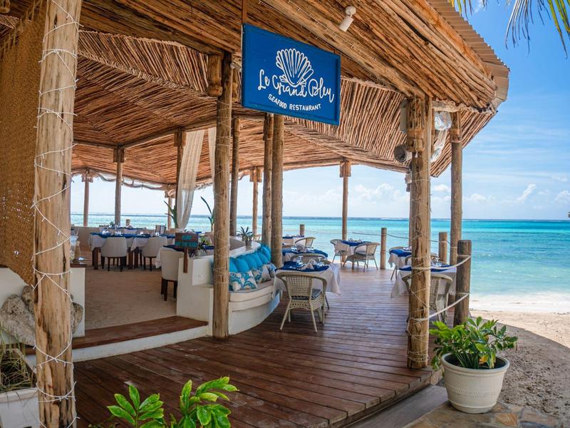 Open strandrestaurant met houten terras, uitzicht op de oceaan en tropische omgeving.