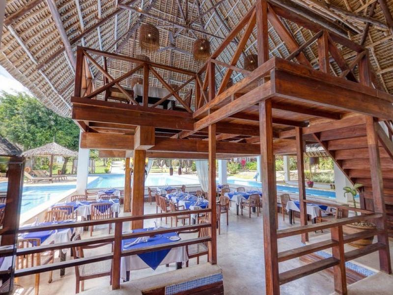 Open woonruimte met houten meubels en uitzicht op hotelzwembad en parasols.