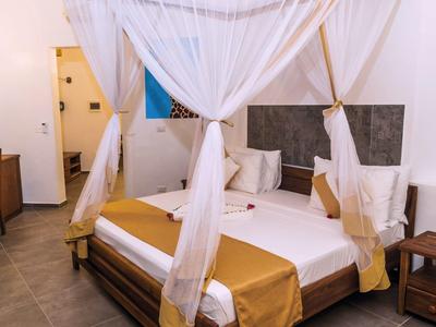 Schlafzimmer mit Himmelbett, weißen Vorhängen, goldfarbenen Kissen und Bettdecke, Holzmöbeln, schlicht.