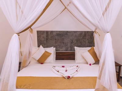 Gemütliches Bett mit weißen und braunen Kissen, Herz aus Blumen und weißen Vorhängen umrahmt.