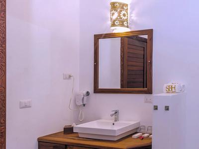 Kleines Badezimmer mit weißem Waschbecken, hölzernem Unterschrank, rechteckigem Spiegel und weißer Wand.