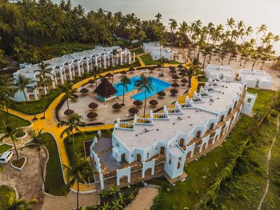 Großes Resort mit weißem Gebäude, blauem Pool, Palmen und grünen Grasflächen am Strand.