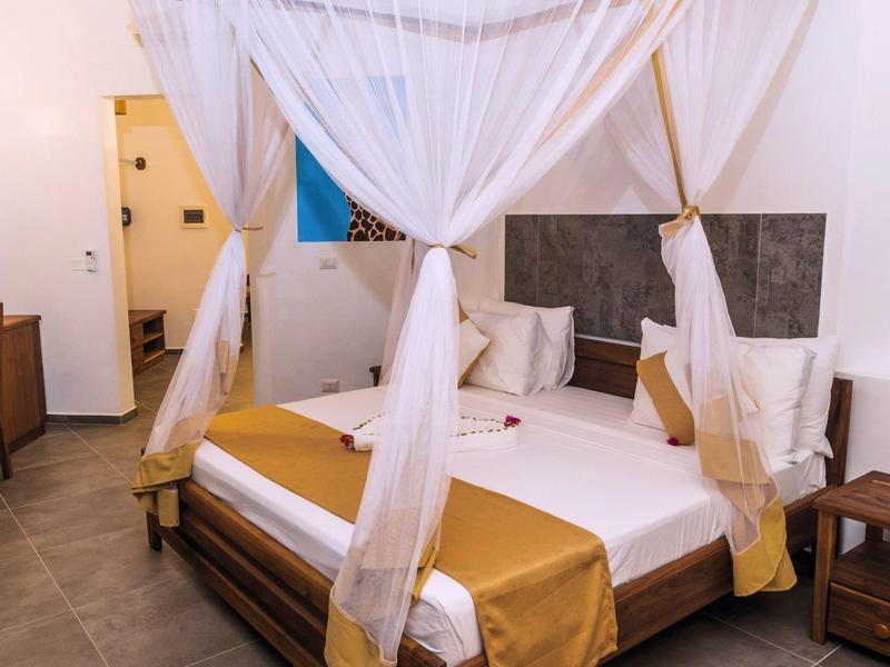 Een hotelkamer met een tweepersoonsbed en witte muskietennetten, ingericht met houten meubels.