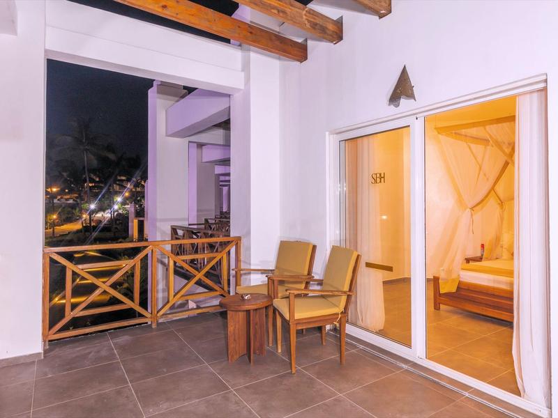 Balkon met houten meubels en nachtelijke stadslichten, grenzend aan een verlichte slaapkamer.