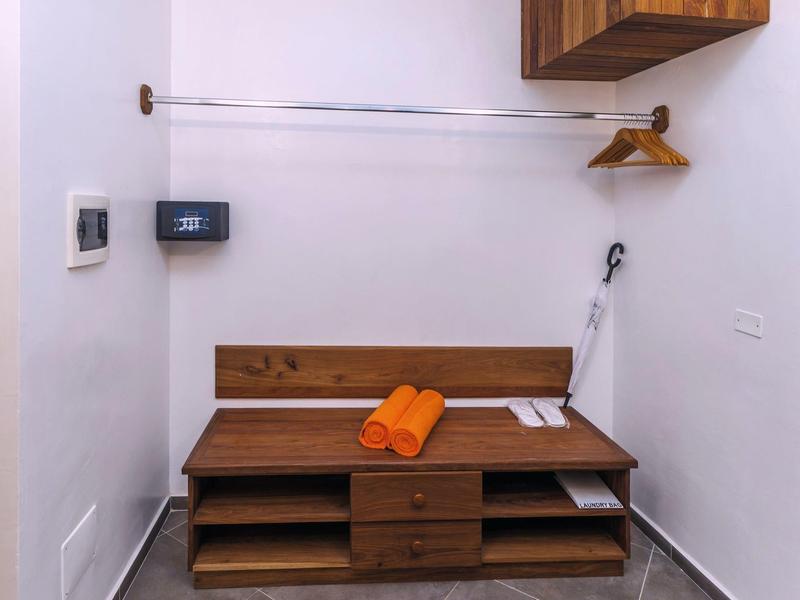 Kleine lichte kamer met houten meubels, twee oranje handdoeken en wandhaken.