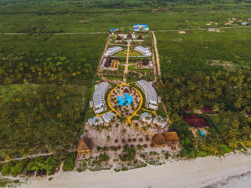 Luchtfoto van een resort met zwembad te midden van groen vlakbij het strand.