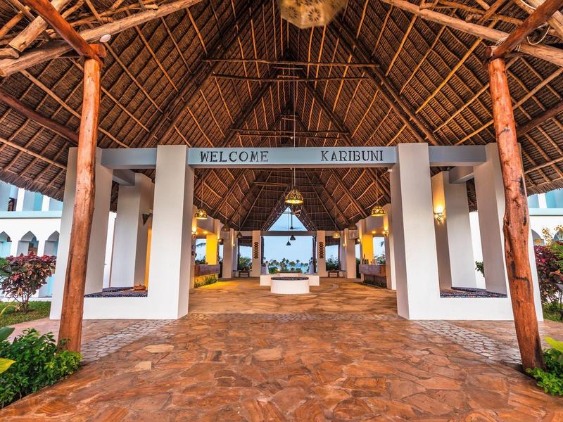 Open entree met rieten dak en uitzicht op zee bij een vakantieresort.