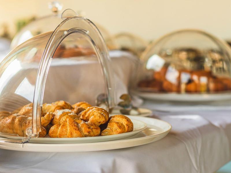 Diverse croissants en gebak onder doorzichtige kappen op een buffet.