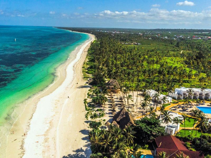 Lang wit zandstrand naast turquoise zee en bebost resort met zwembad.