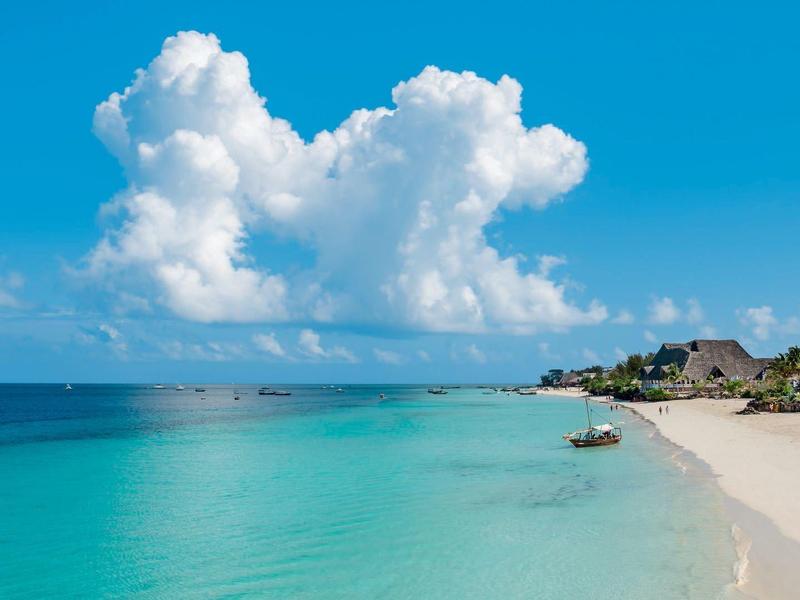 Wit zandstrand met turquoise water en blauwe lucht, verspreide boten en hotelgebouwen.