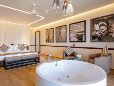 Modernes Hotelzimmer mit Doppelbett, Whirlpool, bequemen Stühlen und stilvollen Wandbildern.