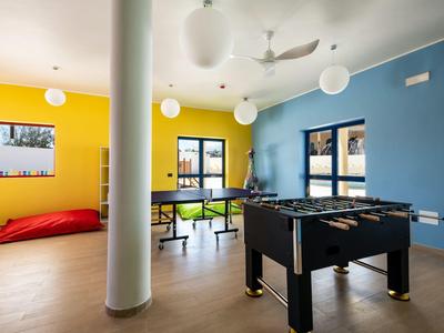 Spielzimmer mit blau-gelben Wänden, Kicker, Tischtennisplatte, Sitzgelegenheiten und großem roten Sitzkissen.