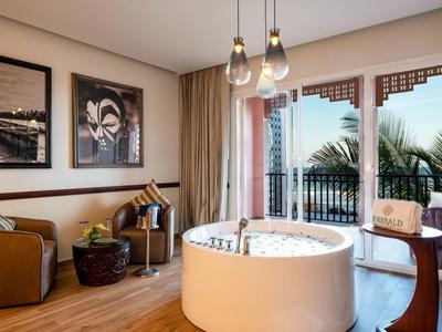 Modernes Hotelzimmer mit Whirlpool, Sofa, Tisch und Balkon mit Palmenblick bei Tageslicht.