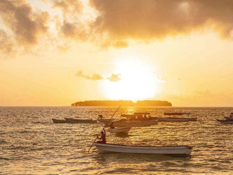 Verschillende boten op kalm water bij zonsondergang met een bewolkte lucht.