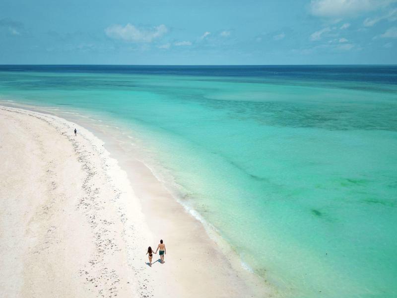 Wit zandstrand met turquoise zee en twee mensen die langs de kust wandelen.