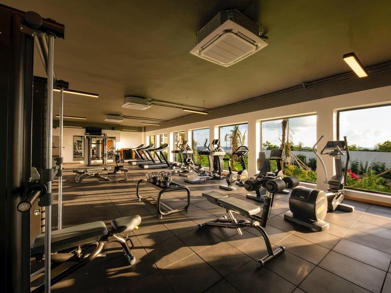 Grote fitnessruimte met diverse trainingsapparatuur en grote ramen met uitzicht op groen.