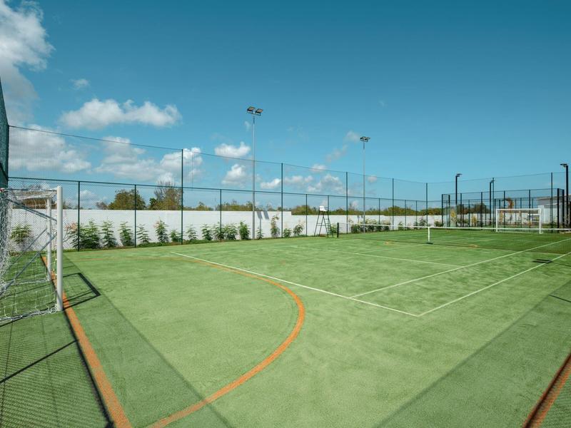 Leeg tennisveld met groen oppervlak en omheining onder blauwe lucht.