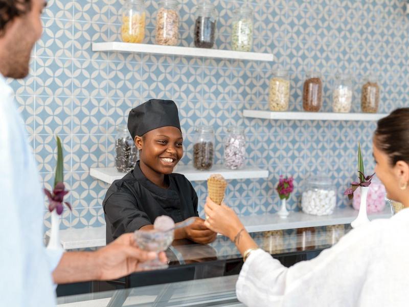 Hotelreceptioniste in kokskleding lacht terwijl ze gasten aan de balie bedient.