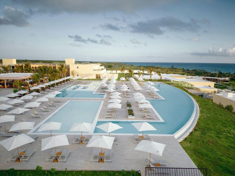 Groot buitenzwembad met witte parasols en uitzicht op de kust bij een hotelresort.