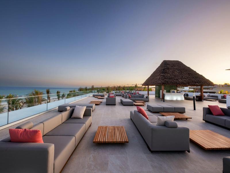 Moderne buitenterras met banken en houten tafels, zeezicht bij zonsondergang.