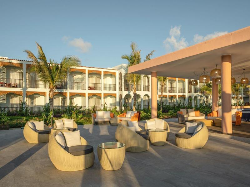 Moderne hotelterras met ronde zitmeubels, palmbomen en een lichte restaurantgedeelte.