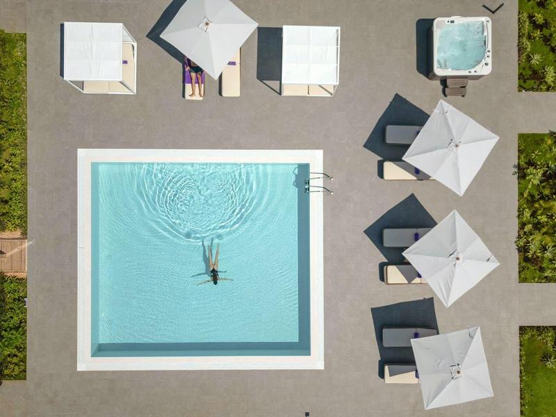 Luchtfoto van een rechthoekig zwembad met ligstoelen en parasols in een tuin.