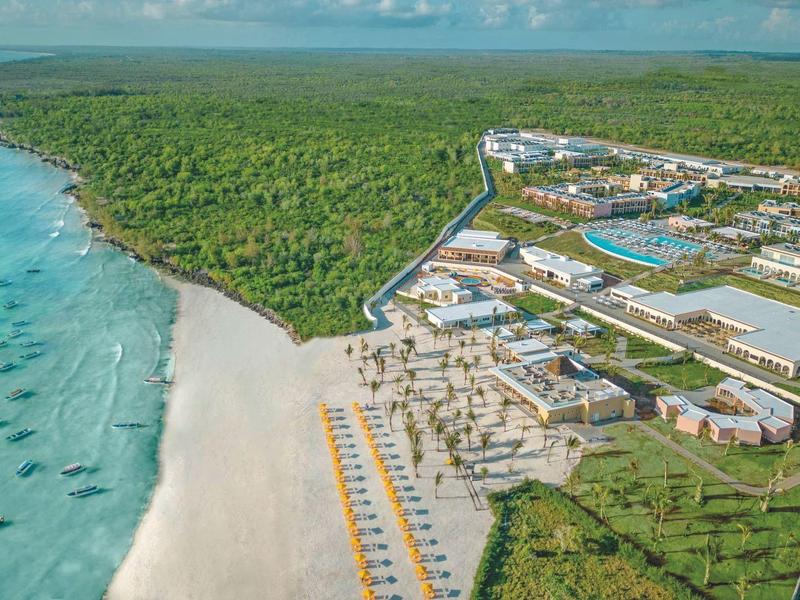 Luxe hotelcomplex met zwembaden en strand aan een beboste kustlijn.