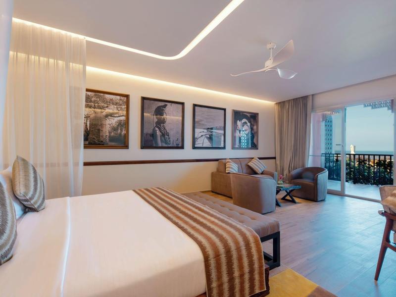 Modern hotelkamer met kingsize bed, zithoek en balkon met zeezicht.