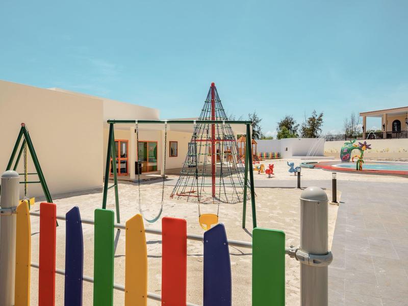 Kleurige omheining rond zonnige speeltuin met glijbanen en klimrekken.