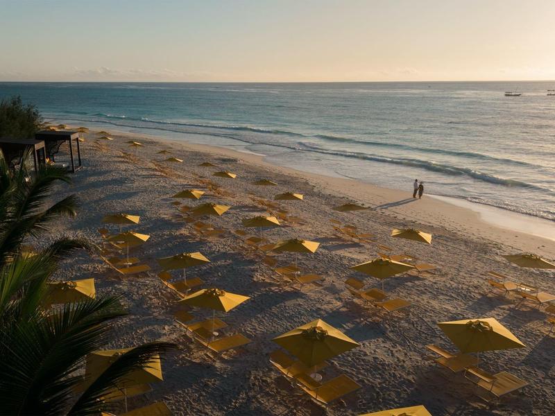 Strand met gele parasols en palmbomen bij zonsondergang