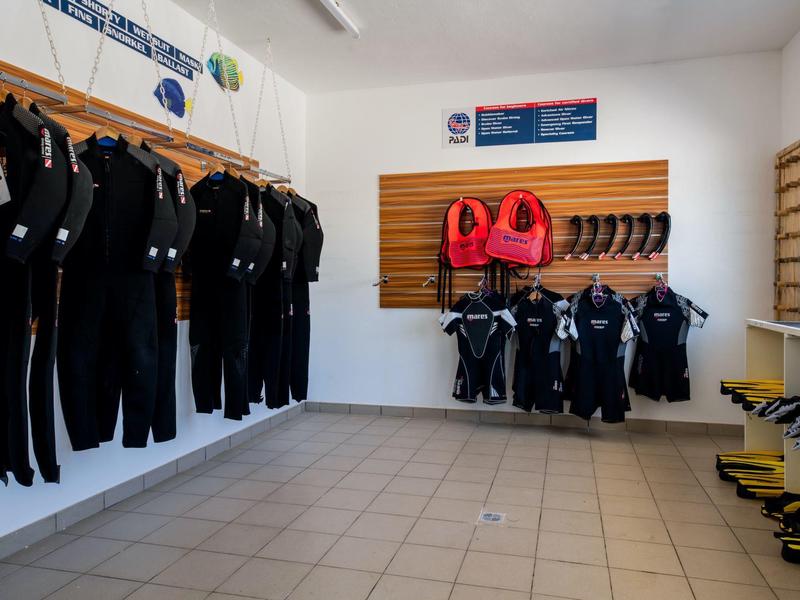 Ruimte met zwarte wetsuits, rode zwemvesten en gele snorkels aan de muren.