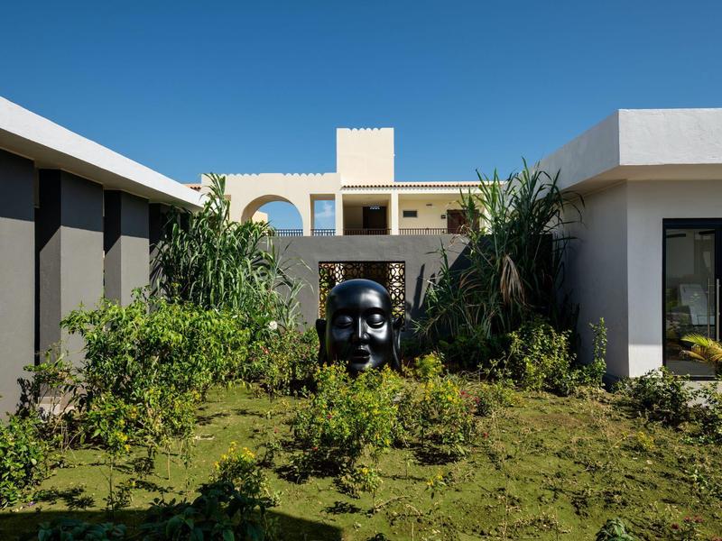 Modern gebouwcomplex met tuin en een zwarte sculptuur in het midden.