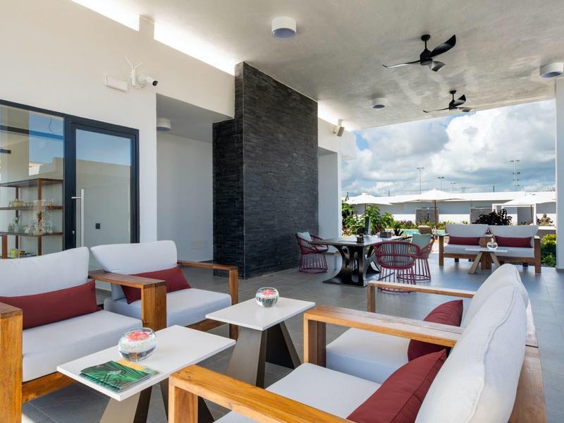 Moderne hotelkamer met houten meubels, witte kussens en uitzicht op terras en lucht.