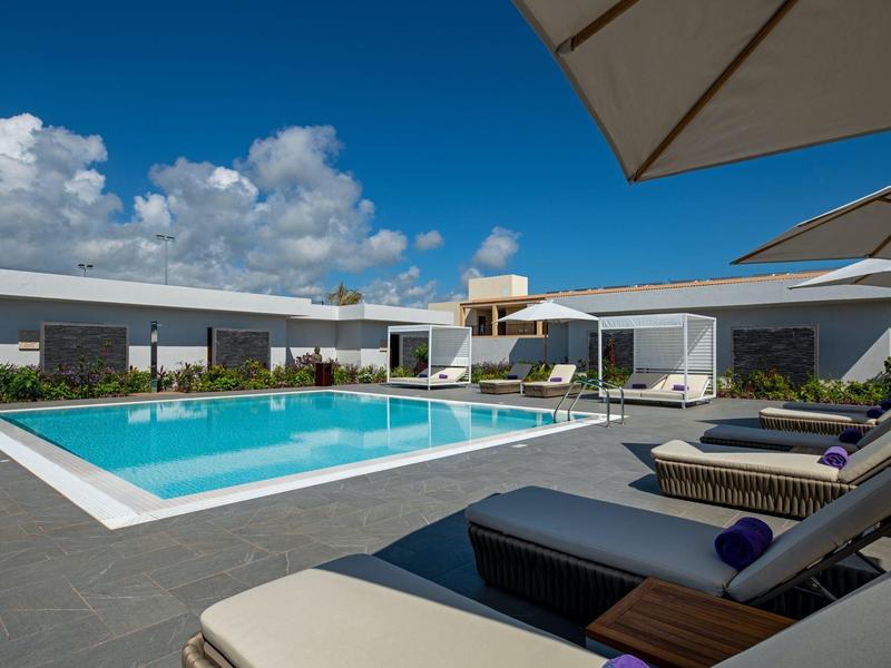 Modair buitenzwembad met ligstoelen en parasols onder een heldere hemel.