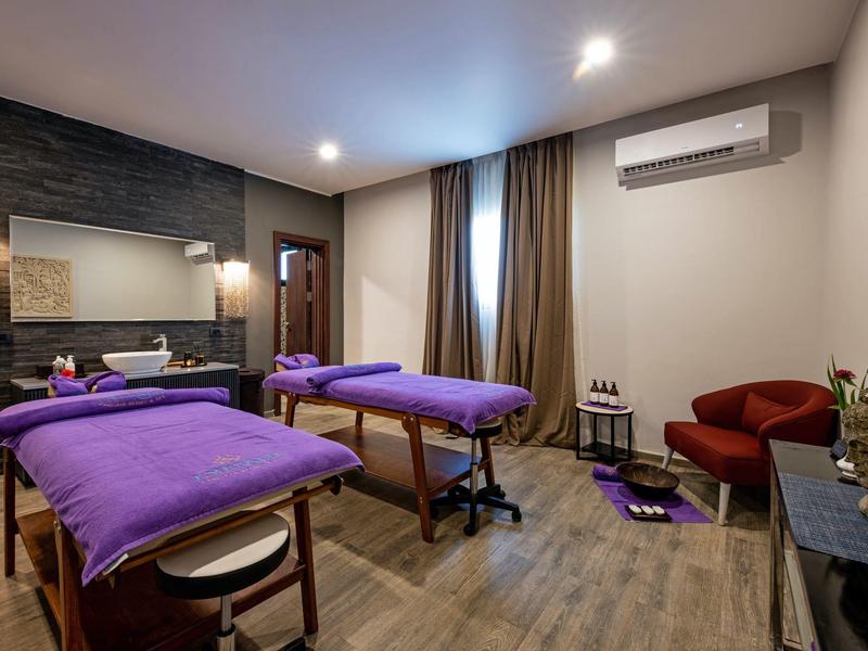 Ontspanningsruimte met twee massagetafels, paarse hoezen en een rustige spa-sfeer.