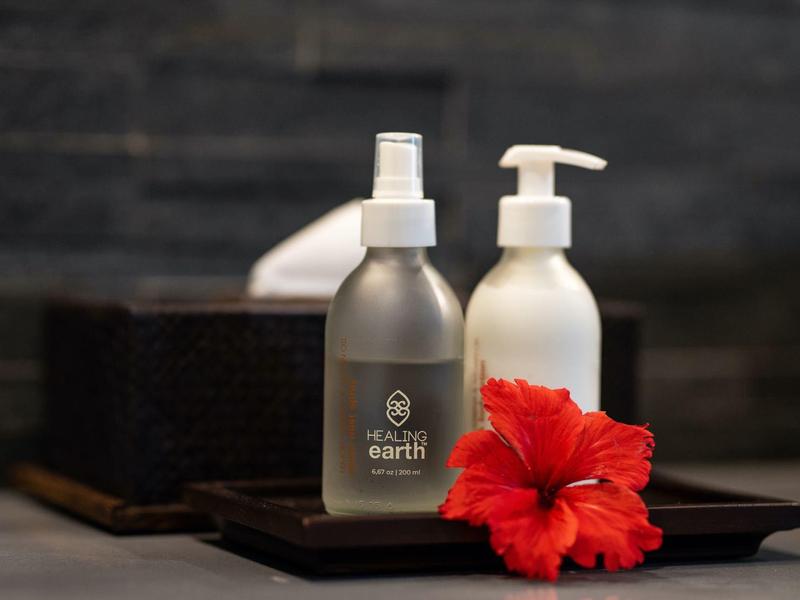 Twee cosmeticaflessen met rode hibiscusbloem op zwart dienblad tegen donkere grijze achtergrond