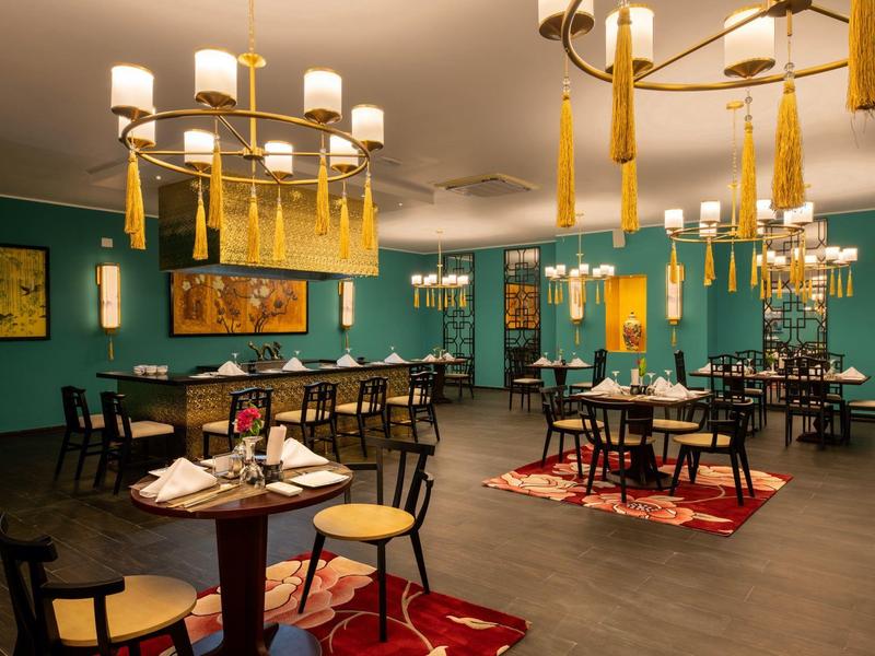 Modern restaurant met groene muren, houten stoelen en grote gouden kroonluchters