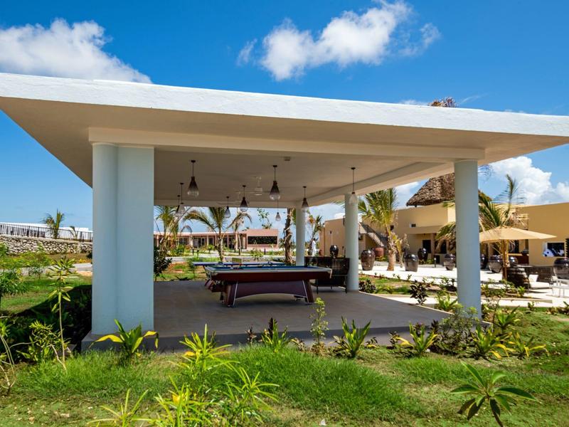 Vrijstaande overdekte buitenruimte met biljarttafel in een tuin bij heldere lucht.