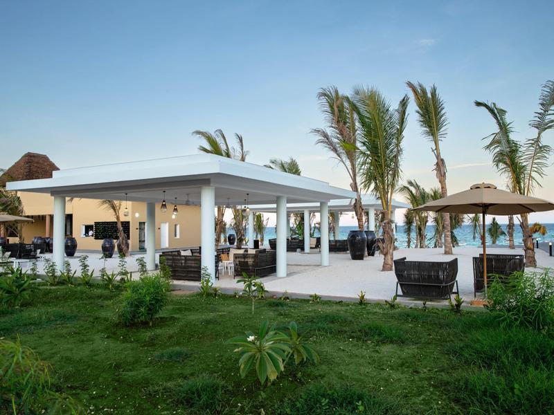 Modern paviljoen met zitgedeeltes naast gras en palmbomen in tropisch resort.