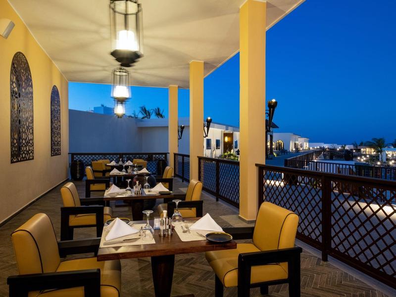 Diner op een terras met gele zuilen en uitzicht op verlichte stad bij schemering.