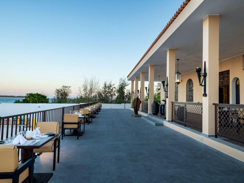 Terras van een hotel met tafels en stoelen met uitzicht op een waterweg bij zonsondergang.
