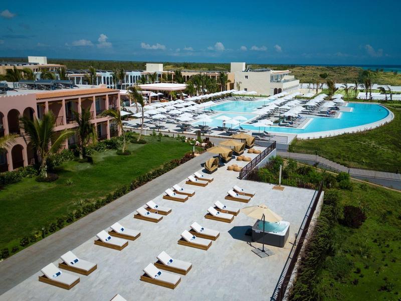 Luxe resort met zwembad, ligbedden en uitzicht op zee op een zonnige dag.