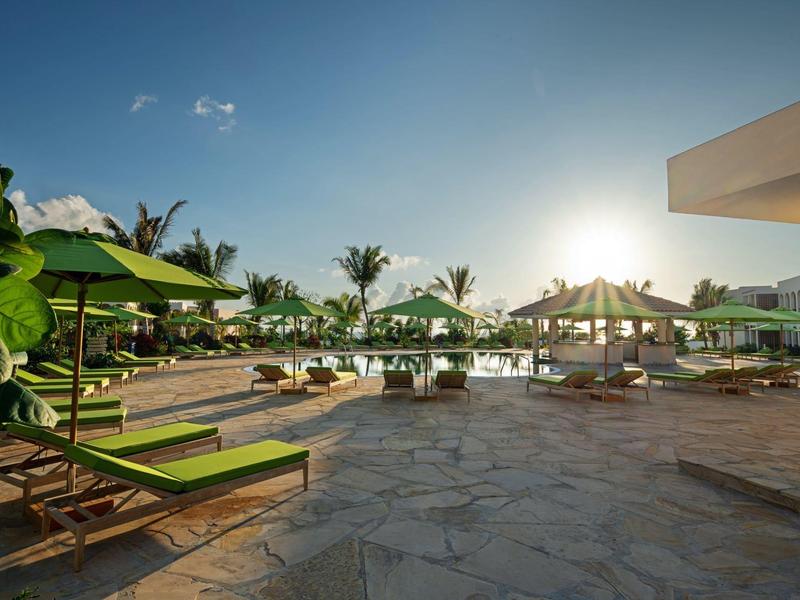 Zonsondergang boven een hotelzwembad met ligbedden en groene parasols.