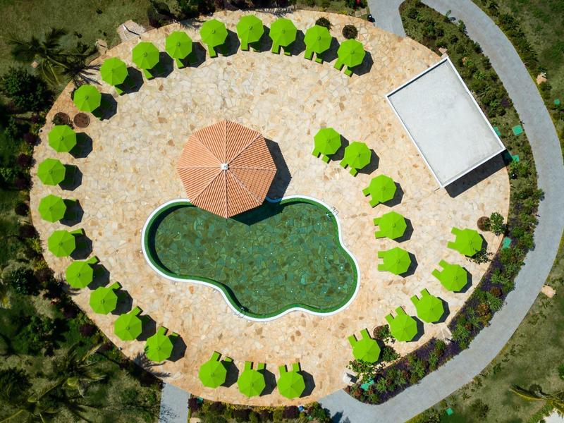 Ronde zwembadomgeving met parasols en een centraal paviljoen, omgeven door groen.