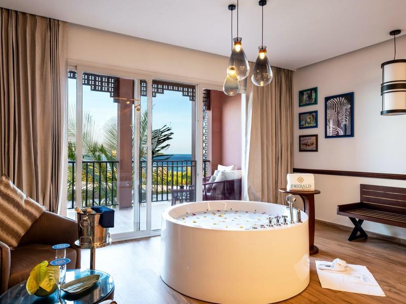 Licht hotelkamer met jacuzzi, balkon en zeezicht bij daglicht.