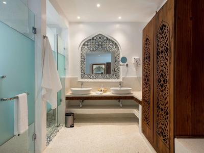 Elegantes Badezimmer mit Doppelwaschbecken, Spiegel mit Ornamentrahmen und Holzschrank mit Schnitzereien.