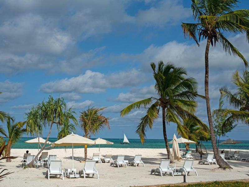 Playa con tumbonas, sombrillas y palmeras en un día nublado junto al mar.