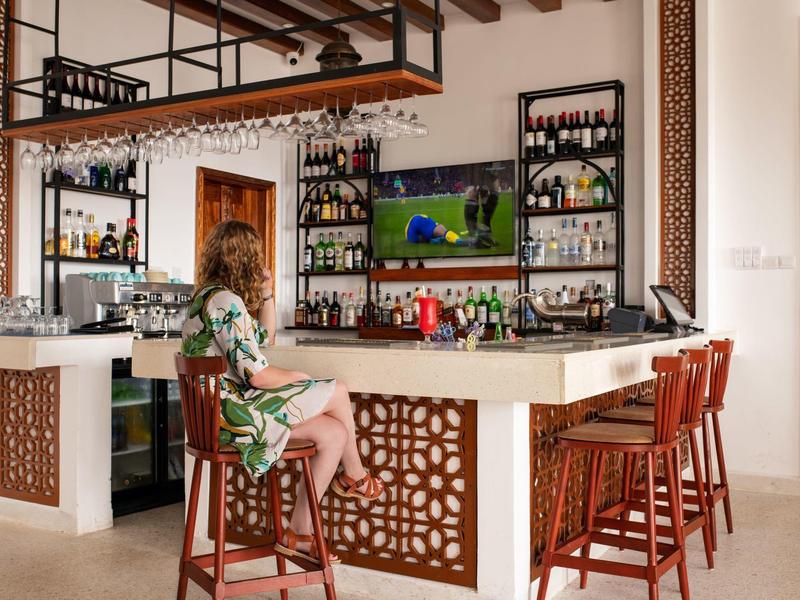 Bar moderna de hotel con taburetes de madera y una mujer viendo la televisión.